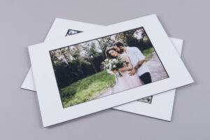 A photo of a couple embracing outdoors, the woman holding a bouquet, is placed on top of another similar photo, both with white borders.
