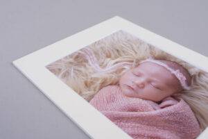Framed photo of a sleeping baby wrapped in a pink blanket, lying on a fluffy surface, with a small headband.