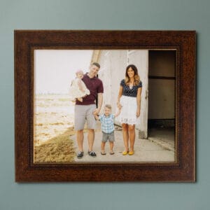 Framed portrait of a smiling family with a father, mother, young son, and baby in front of a rustic building.