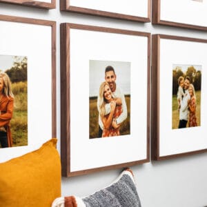 Wall display of family photos in wooden frames above a couch with yellow and gray pillows.