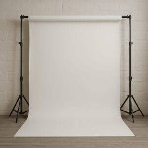 A plain white photography backdrop with professional tripod stands is set up in a studio with light wooden flooring and a textured white wall.