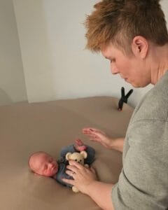 An adult tends to a sleeping baby lying on a soft surface, with a small teddy bear beside the baby.