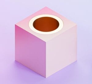 A pink cubic object with a circular hole on top sits on a light purple surface.