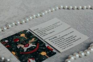 Three cards lie on a gray surface with a string of pearls; two cards have dictionary-style definitions, and one card has a holiday-themed rocking horse design.
