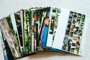 A stack of printed photographs spread out on a light-colored textured surface, showing various images and photo contact sheets.