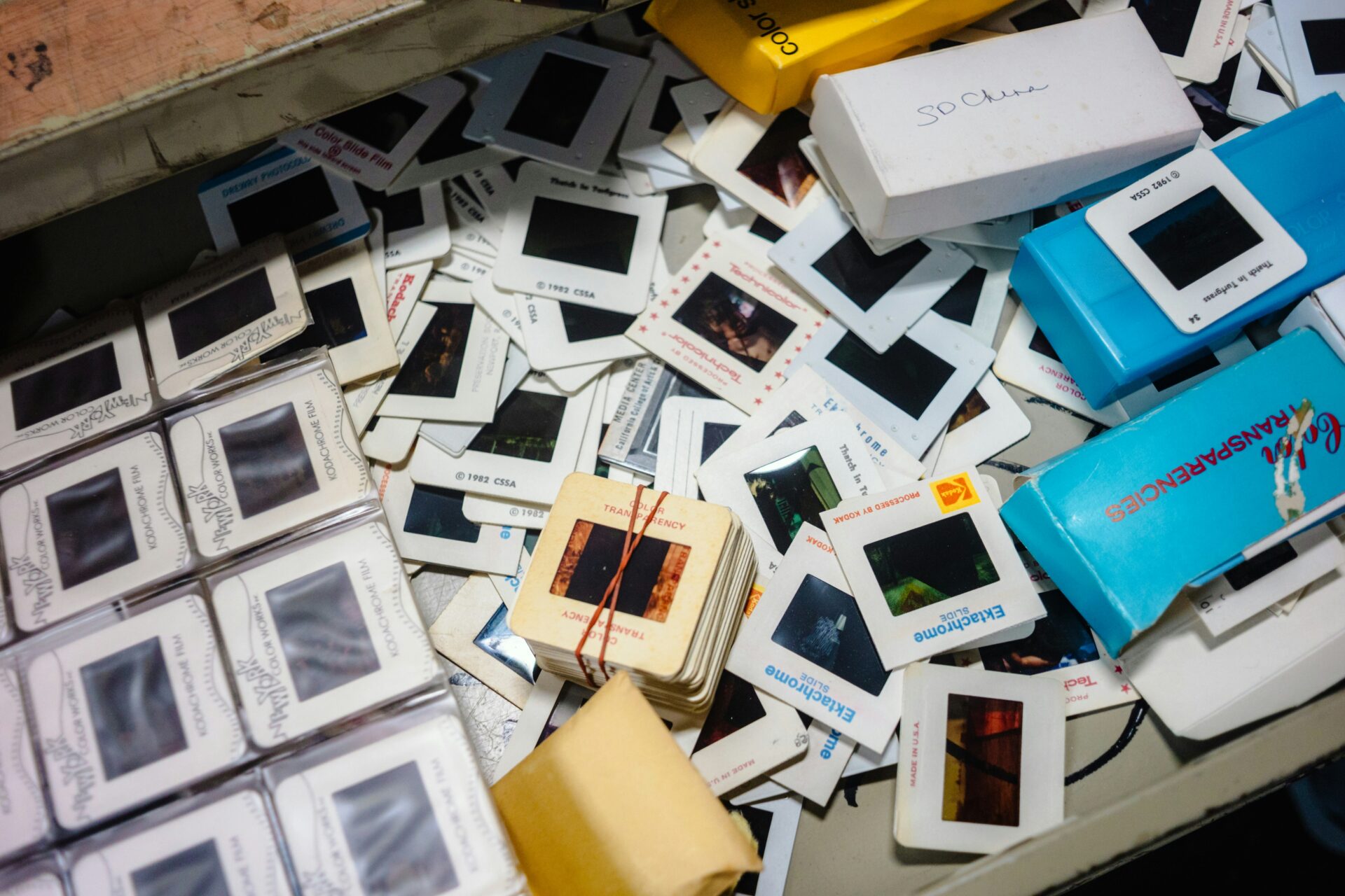 Scattered photographic slides and film transparencies are shown in a drawer, some loose and some in stacks, with a few boxes labeled "Ektachrome" and "Transparencies.
