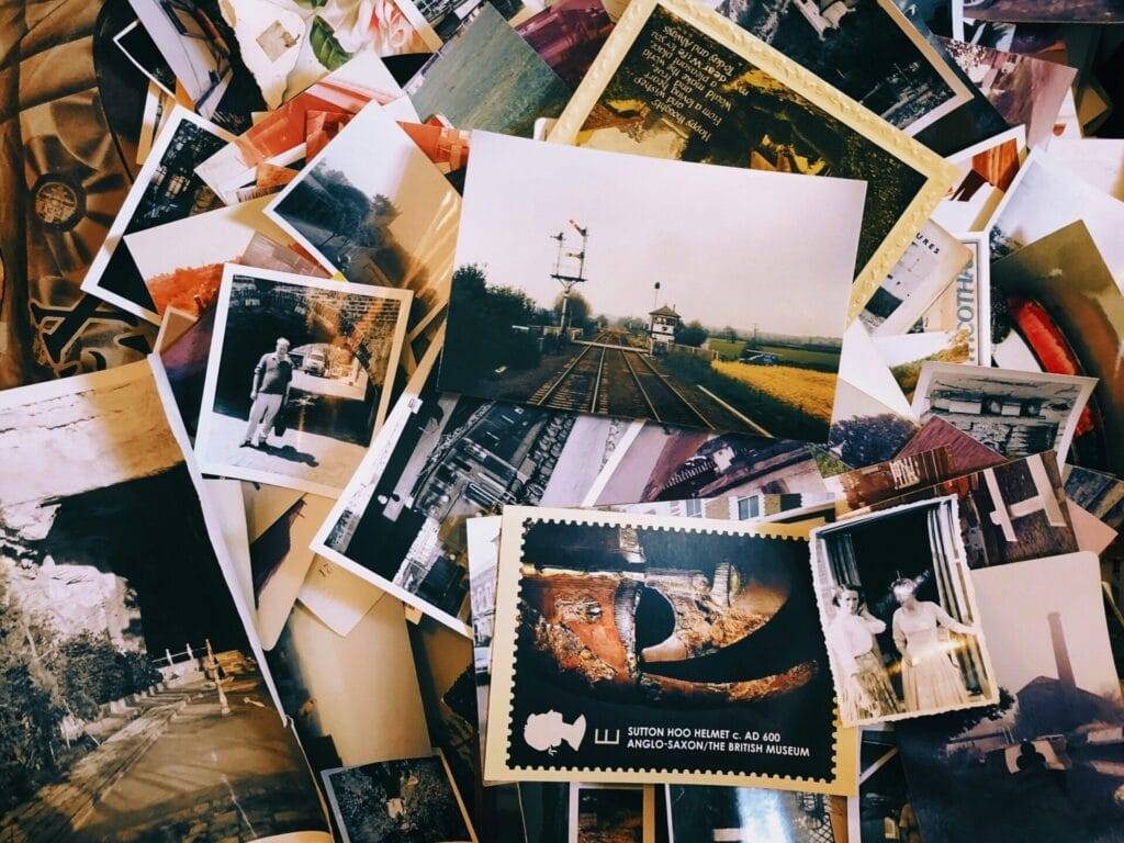 A pile of assorted vintage photographs and postcards, some in color and some in black and white, scattered and overlapping each other.