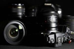 A close-up view of several Canon camera lenses and a Canon DSLR camera body arranged on a black surface.