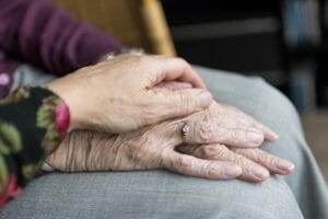A younger hand gently rests on top of an older person's hands, one of which has a ring, symbolizing comfort and support.