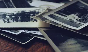 A stack of vintage black and white photographs lies scattered on a wooden surface.