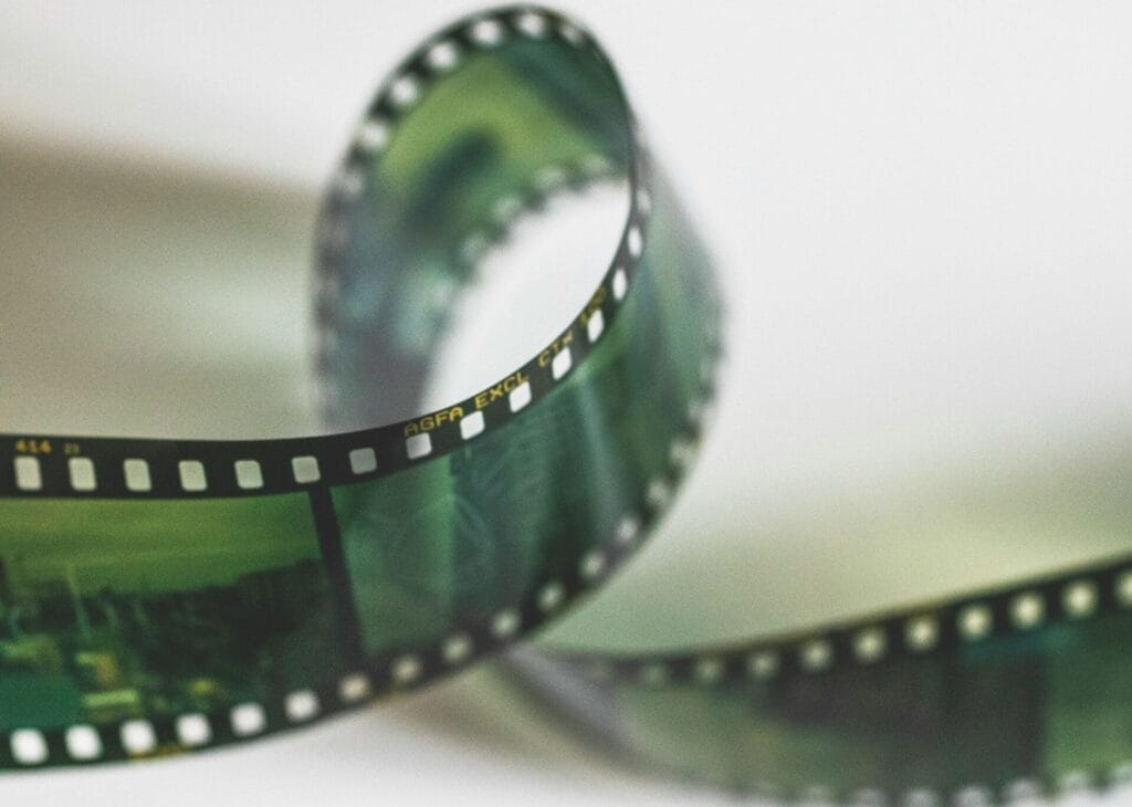 A close-up of a curled strip of photographic film, showing sprocket holes and some faint images on the negatives.