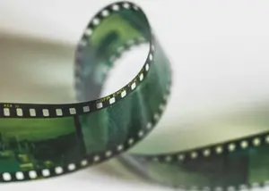 A close-up of a curled strip of photographic film, showing sprocket holes and some faint images on the negatives.