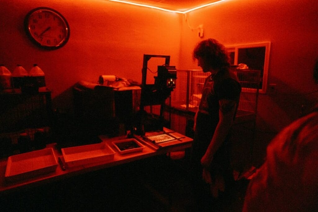 Photographer using an enlarger to make a print from 35mm film in a darkroom