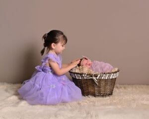 Toddler tenderly touching a newborn sibling's head in a basket