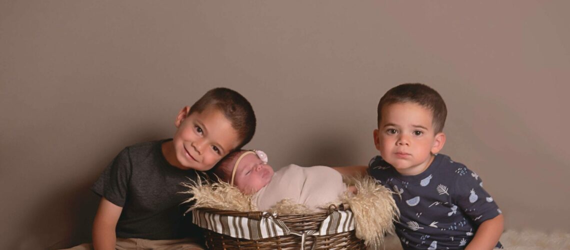 Three boys sitting in a basket with a newborn in it.