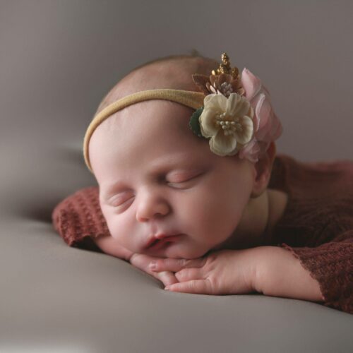 A newborn baby girl posed on her hands in the studio