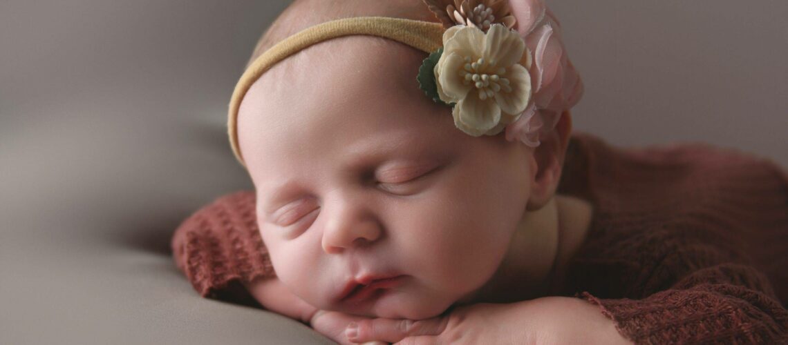 A newborn baby girl posed on her hands in the studio