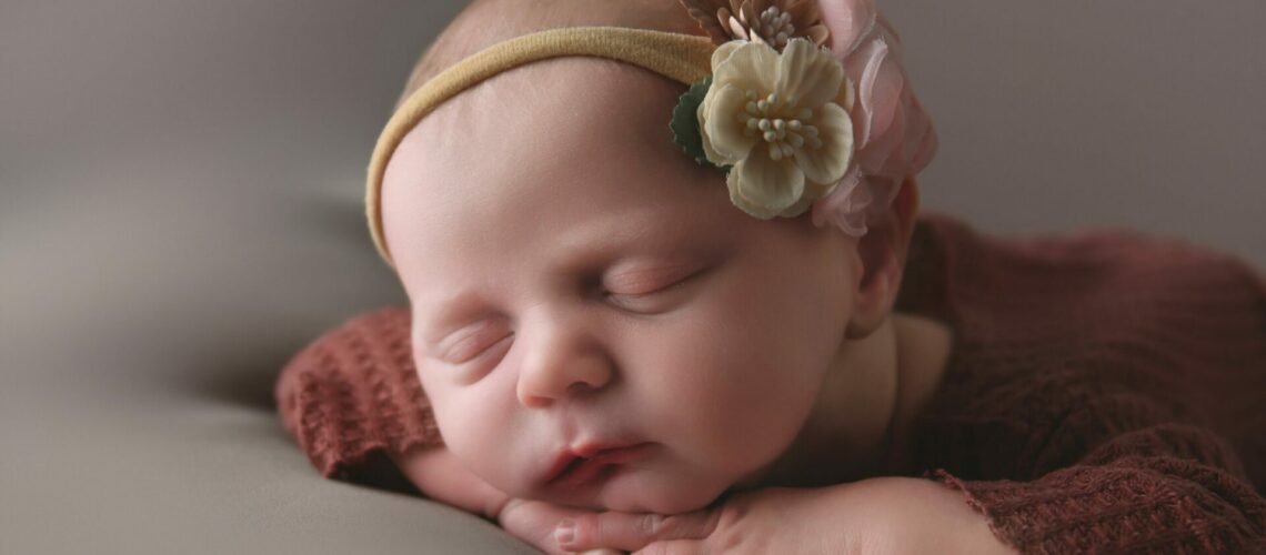 A newborn baby girl posed on her hands in the studio