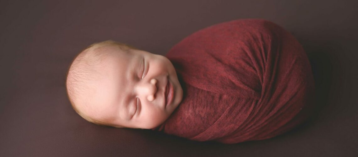 A newborn baby boy wrapped in a red wrap.