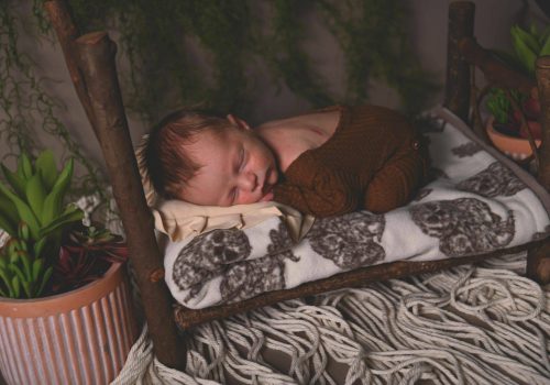 00002_C_021 a newborn sleeping on a wooden bed with a patterned blanket with macrame floor. Saint paul minnesota