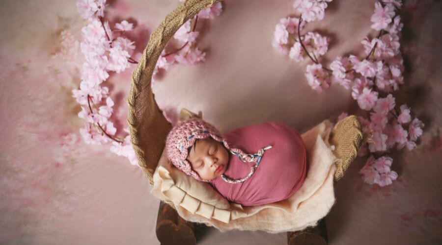 A newborn baby is laying in a pink basket with cherry blossoms.