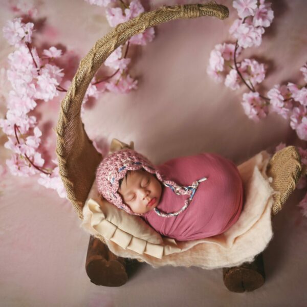 A newborn baby is laying in a pink basket with cherry blossoms.