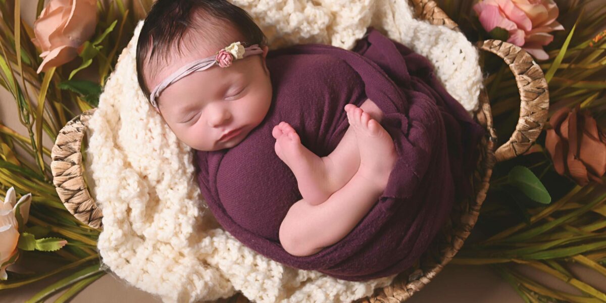 A newborn girl sleeping in a basket with flowers.