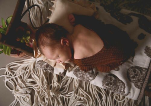a newborn sleeping on a wooden bed with a patterned blanket with macrame floor. Saint paul minnesota