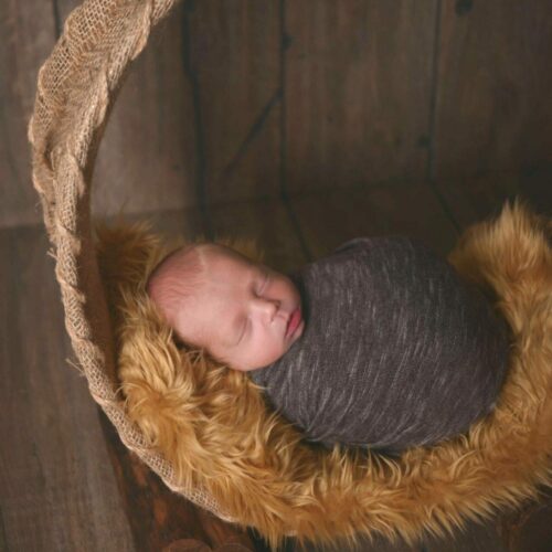 A newborn sleeping in a wicker basket on a wooden floor.