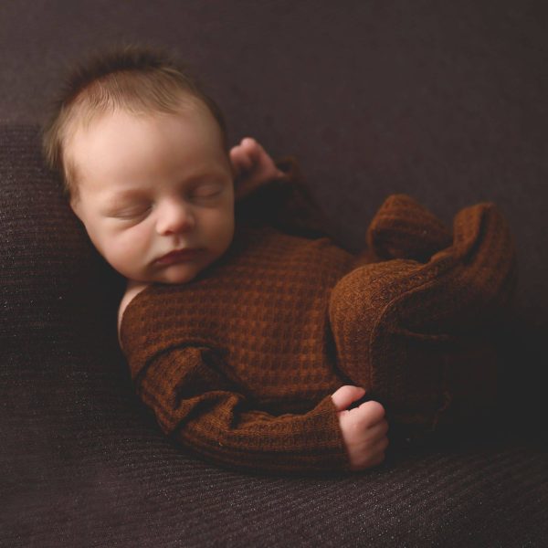 00004_C_023 a newborn sleeping on a blanket on a brown surface.