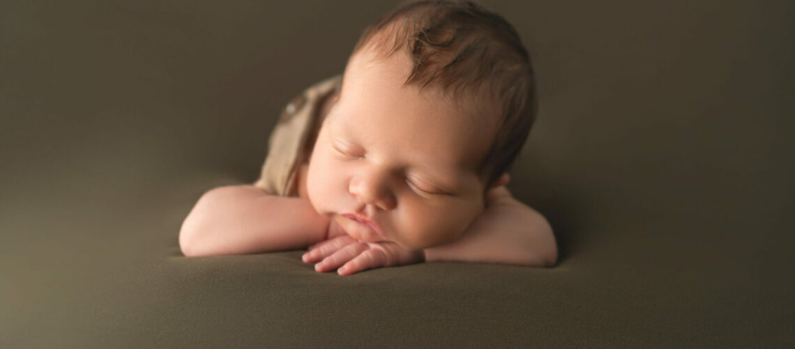 A baby boy is laying down on a brown background.