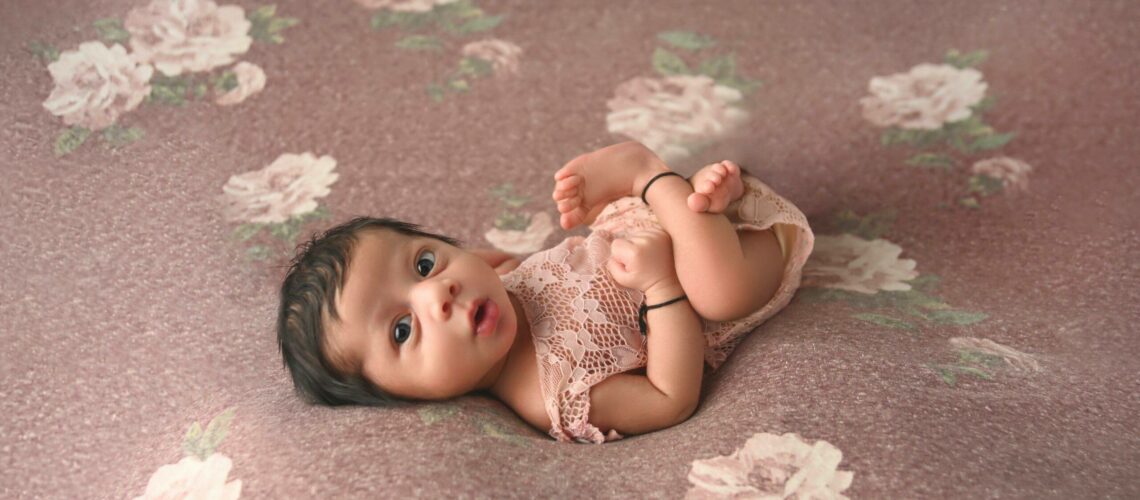 A baby girl laying on a pink floral background.