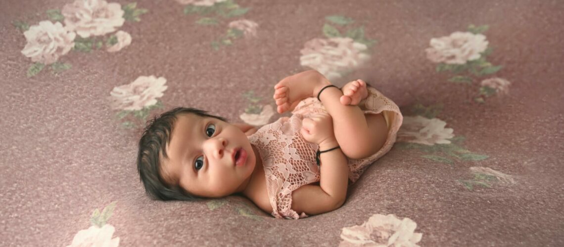 A baby girl laying on a pink floral background.