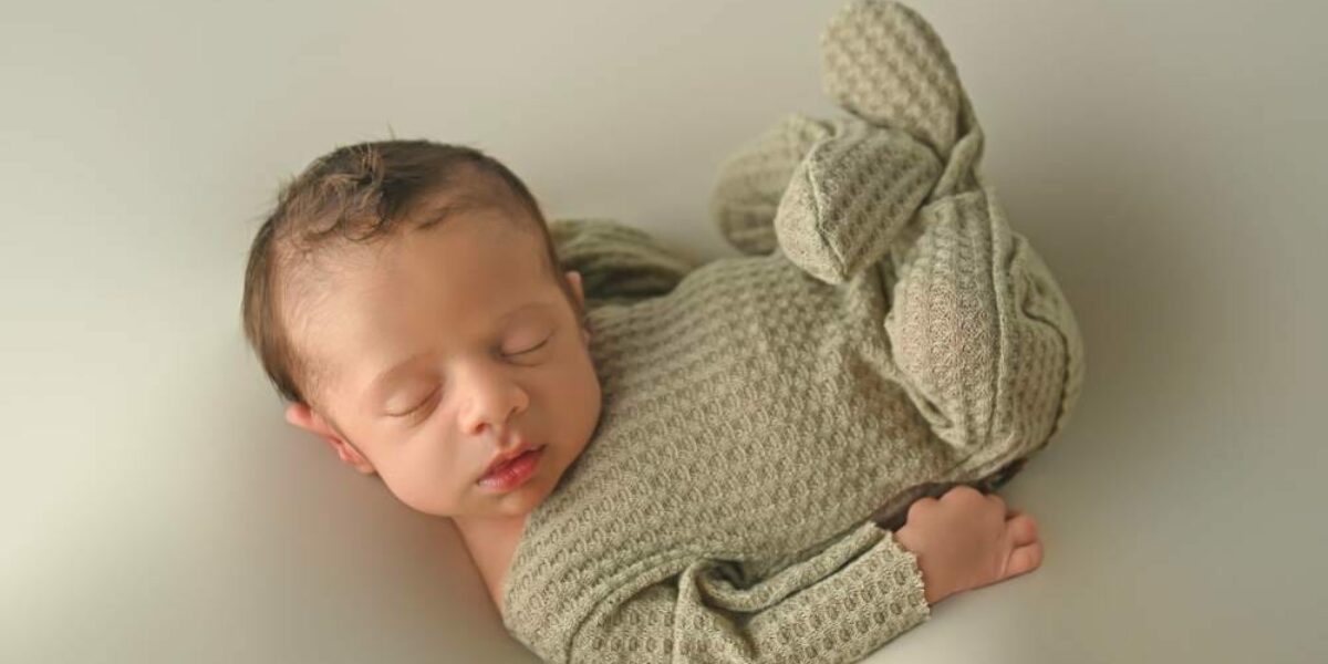 A baby boy is laying on a grey background.