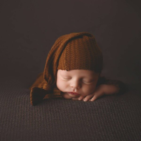 00005_C_031 a newborn sleeping on a blanket on a brown surface with a hat on
