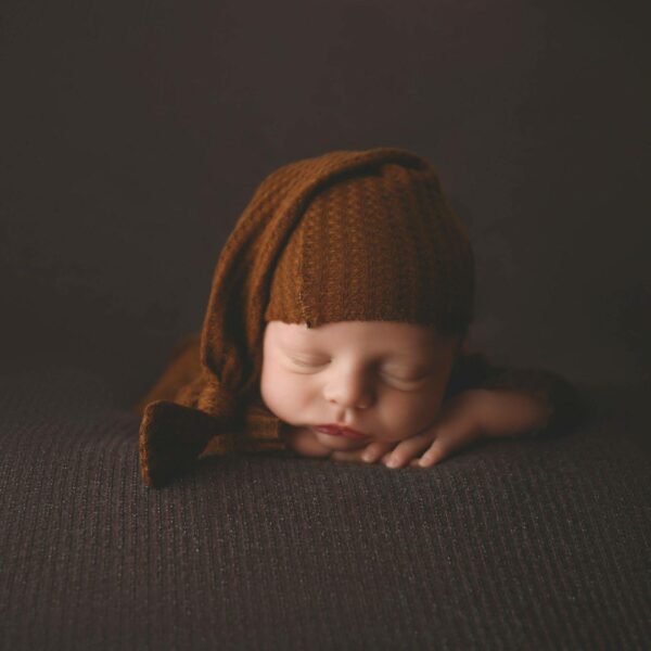 a newborn sleeping on a blanket on a brown surface with a hat on