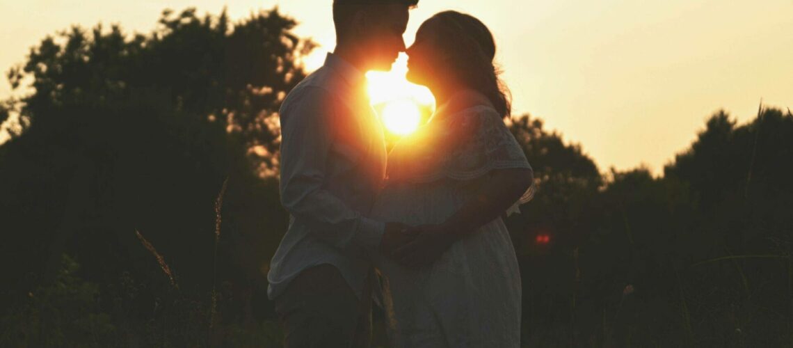 A couple kisses at sunset in a field.