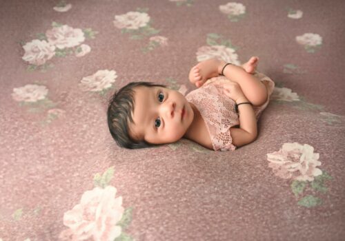A baby girl laying on a pink floral background.