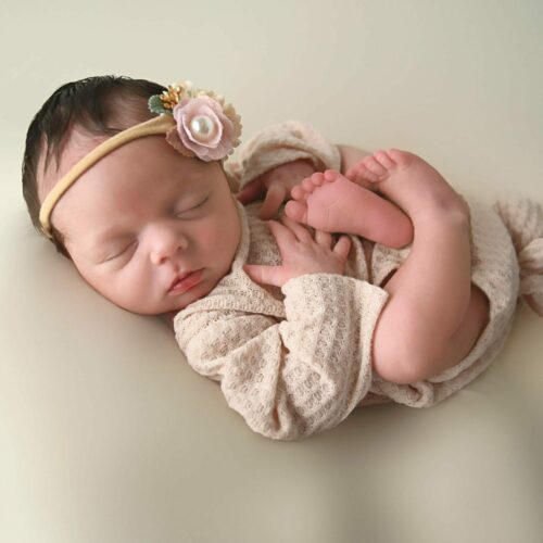 A newborn baby girl is laying down on a white background.