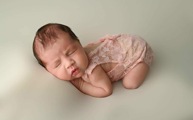 A baby girl in a pink outfit is laying on a white background.