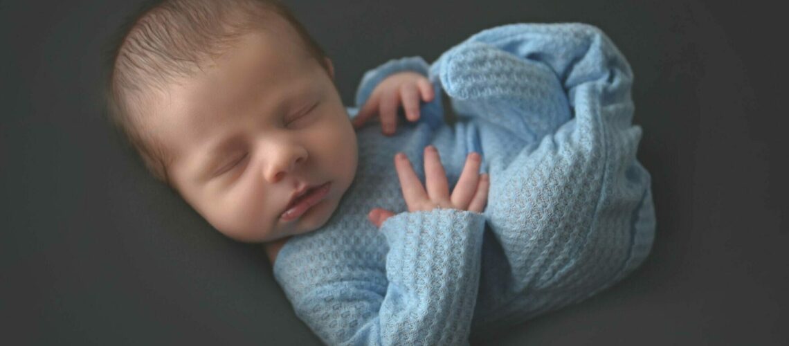 A newborn baby boy is laying on a dark background.