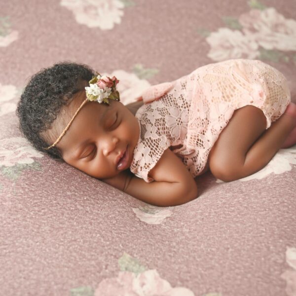 A baby girl is sleeping on a pink background.