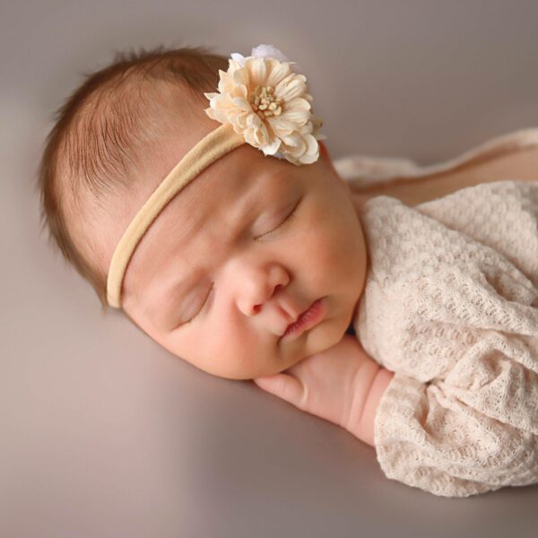 A baby girl sleeping with a flower headband on her head.