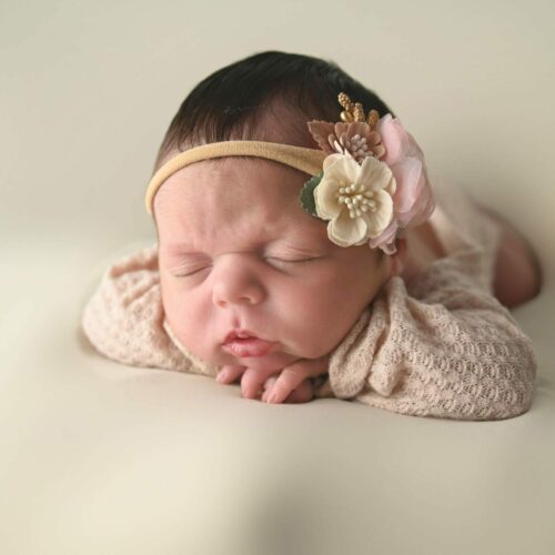 A baby girl is laying on a white background with a flower headband.