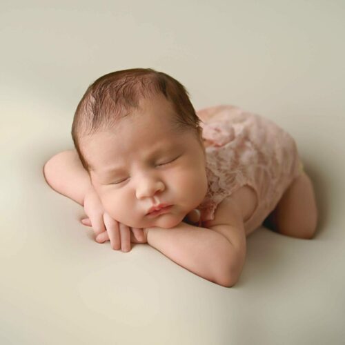 A baby girl is laying down on a white background.