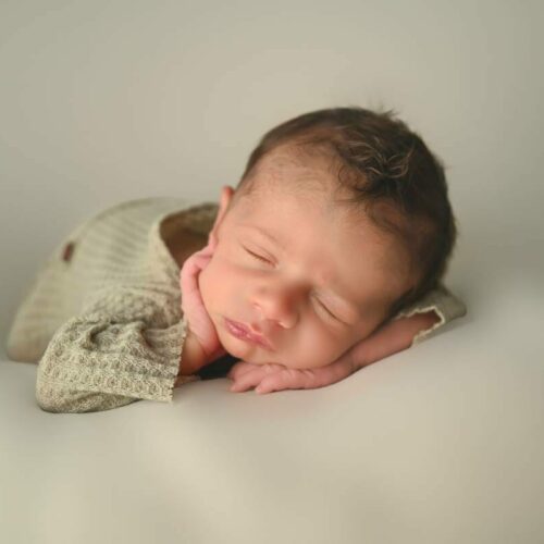 A baby boy is laying on a white background.