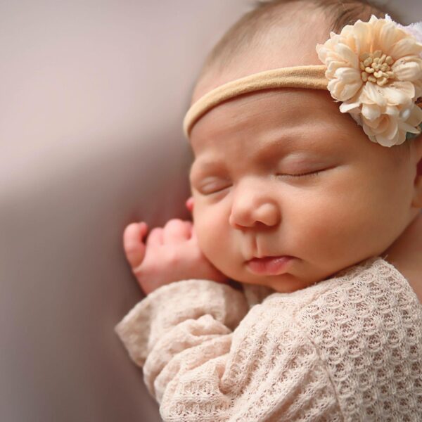 newborn baby with headband laying on cream blanket