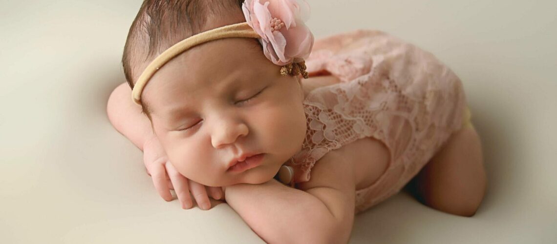 A baby girl is laying on a bed with a pink headband.