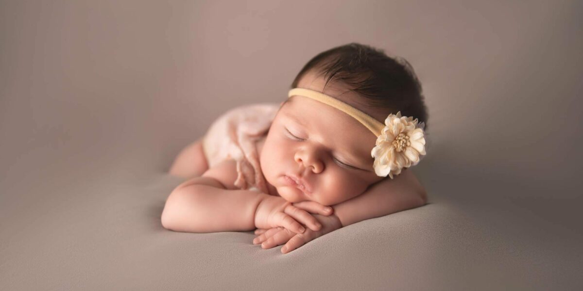 A baby girl laying on a grey background with a flower headband.