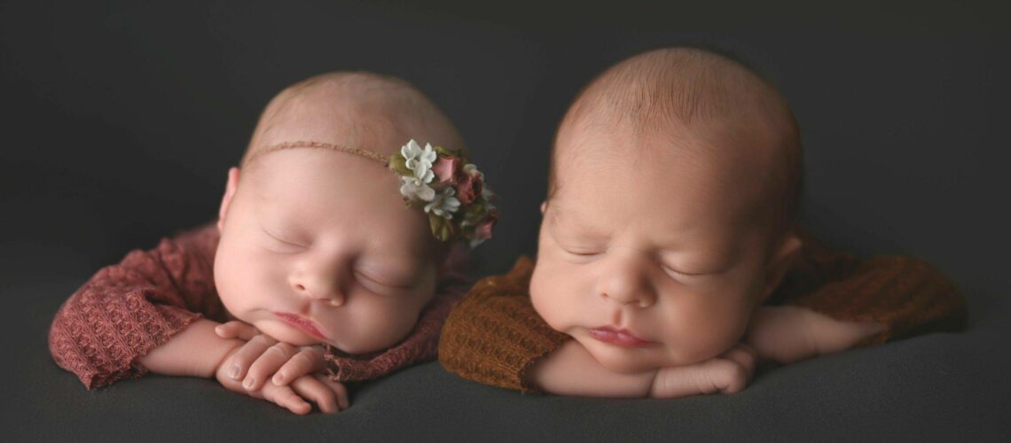 twin babies, with head on hands, asleep on grey background, posing for their newborn photography session